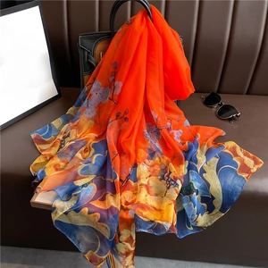 Elegant floral print silk shawl in vibrant orange and blue draped over a black handbag