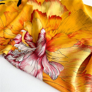 Detailed texture of bright yellow silk square scarf with vibrant orange floral patterns