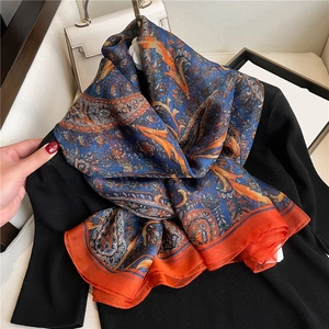 Close-up of luxury navy blue silk scarf with classic orange paisley floral patterns