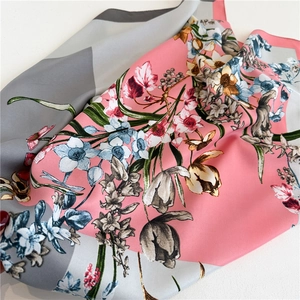 Close-up of elegant floral print silk scarf with pink and grey pattern on white surface