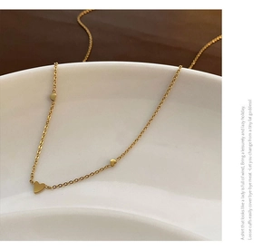 Détail macro du collier doré orné de trois cœurs posé sur une coupelle en céramique blanche