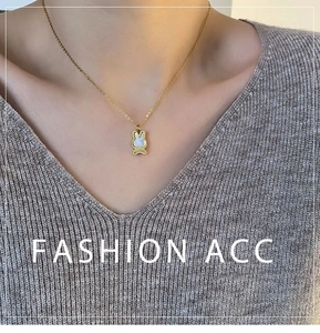 Gros plan d'un collier lapin doré avec nacre porté sur un pull en maille douce