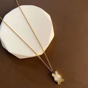 Collier lapin doré avec cœur en nacre blanche posé sur un support en pierre