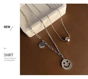 Macro shot of silver cutout smiley pendant necklace with layered bead chains detail