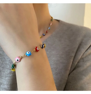 Détail de l'ensemble collier et bracelet œil maléfique coloré sur un pull gris