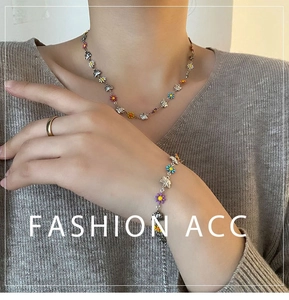 Detail of colorful daisy and butterfly charms on a silver clavicle necklace and bracelet