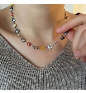 Detail of a titanium steel daisy and butterfly necklace with vibrant enamel charms