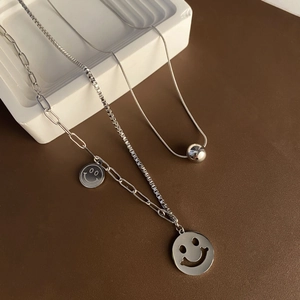 Silver hollow smiley face pendant necklace and silver bead chain on leather background