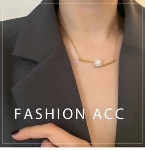 Detail of a gold minimalist necklace with a curved bar and white pearl on a female model