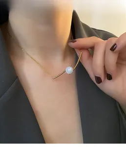 Detail of minimalist gold choker with arched bar and iridescent pearl on grey blazer