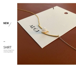 Detail of elegant gold-toned collar necklace with curved bar and white pearl pendant