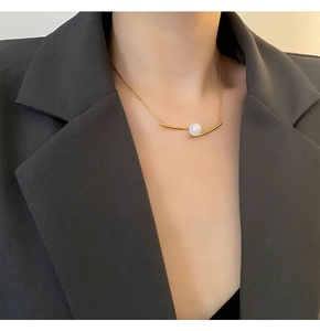 Detailed close-up of a minimalist gold pearl necklace worn over a grey blazer jacket