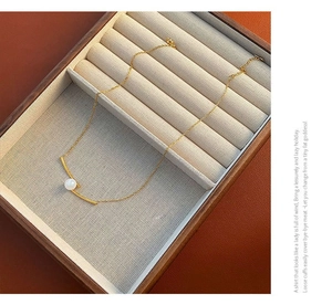 Detailed view of a gold titanium necklace with a curved bar and white pearl in a jewelry box