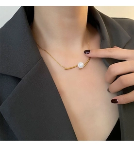Detail of a gold titanium steel necklace featuring a curved bar and white pearl on model