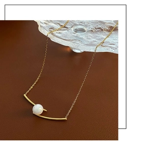Detail of gold titanium necklace with curved bar and pearl on brown leather backdrop