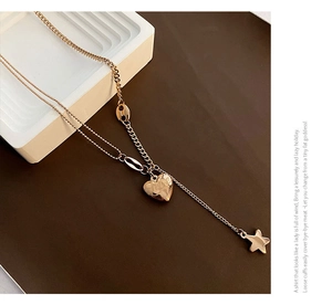 Detail of gold double-layered necklace with heart and star charms on a white pedestal