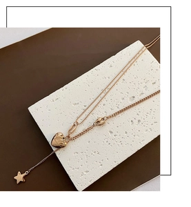 Close-up of rose gold double-layered necklace with heart and star pendants on a stone block