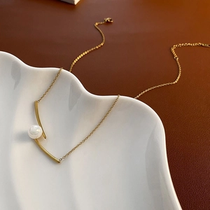 Elegant gold titanium steel cross necklace with a central pearl on a ceramic plate