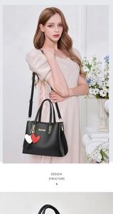 Detail of black lychee grain leather tote bag with gold logo and heart charm on a model