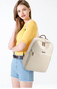 Detail of a beige lightweight backpack with a brown leather handle and metal logo plaque
