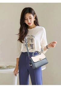 Detail of color-block handbag in misty blue and cream with golden clasp and bear charm