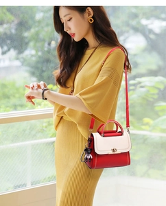 Close-up of red and beige handbag featuring golden ring lock and black bear charm