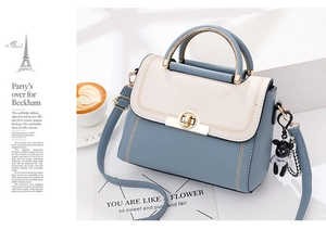 Detail of blue and cream leather handbag featuring gold turn-lock and bear charm