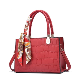 Red crocodile texture handbag with woven handle and elegant scarf on white background
