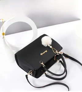 Detail der schwarzen Lederhandtasche mit goldener Hardware und weißem Plüsch-Anhänger