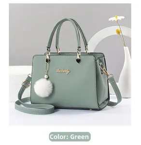 Detail der grünen Lederhandtasche mit Metallgriff, Herzdekor und flauschigem Bommelanhänger