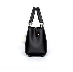 Seitenansicht der schwarzen matten Handtasche mit goldener Hardware und weißem Plüschball
