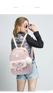 Model wearing a small light pink faux leather backpack with bow and pompom charm