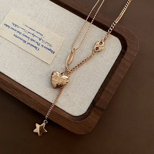 Double-layered gold titanium steel necklace with heart and star pendants on white fabric