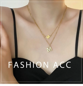 Détail d'un collier double rang en acier titane doré avec pendentifs lettre M en nacre