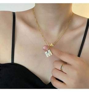 Détail d'un collier doré double rang avec pendentif lettre M en nacre sur le mannequin