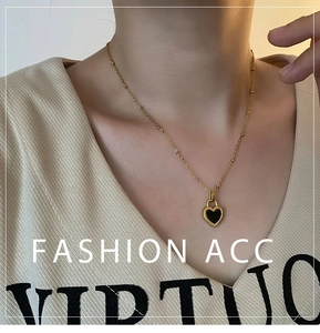 Close-up of golden beaded chain necklace with black heart pendant on beige knitwear
