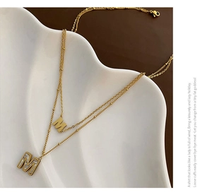 Vue détaillée du collier double doré avec pendentif lettre M en nacre sur plat céramique