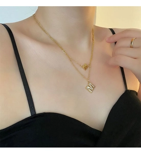 Détail d'un collier double épaisseur en titane doré avec pendentifs M nacrés sur mannequin