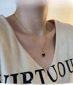 Detail of a gold beaded necklace featuring a black heart-shaped pendant on a model