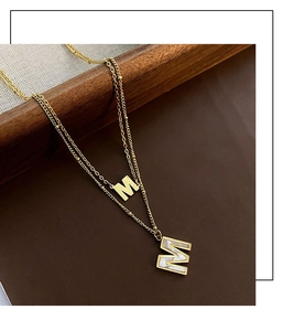 Détail du collier double rang doré avec pendentif M en nacre et chaîne perlée