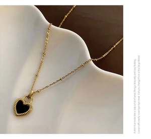 Close-up of gold titanium steel necklace with a black heart pendant on a white ceramic plate