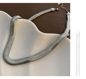Detailed macro view of silver flat snake chain texture with lobster clasp on ceramic plate