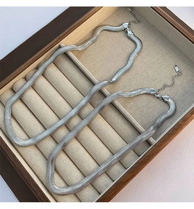 Detailed macro view of flat silver snake chains in a wooden box with lobster clasp closure