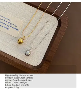 Détail de pendentifs pomme en acier titane or et argent sur un plateau en bois chic