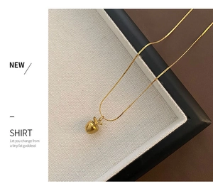Détail d'un collier pendentif pomme dorée polie avec accent de feuille sur surface texturée