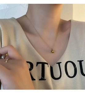 Détail d'un collier pendentif pomme dorée et d'une bague assortie portés par un mannequin