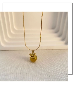 Détail d'un pendentif pomme doré suspendu à une fine chaîne de style minimaliste