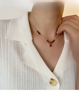 Detail of beaded necklace with ruby red square pendant worn by a model on white shirt