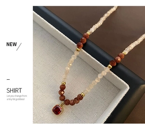 Detail of beaded necklace with cream stones and a square ruby-red pendant in gold setting