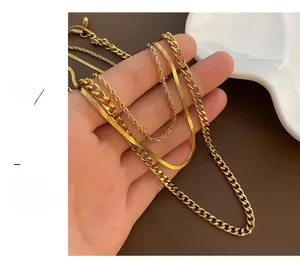 Detailed view of layered gold snake and cuban link chain necklaces held in hand